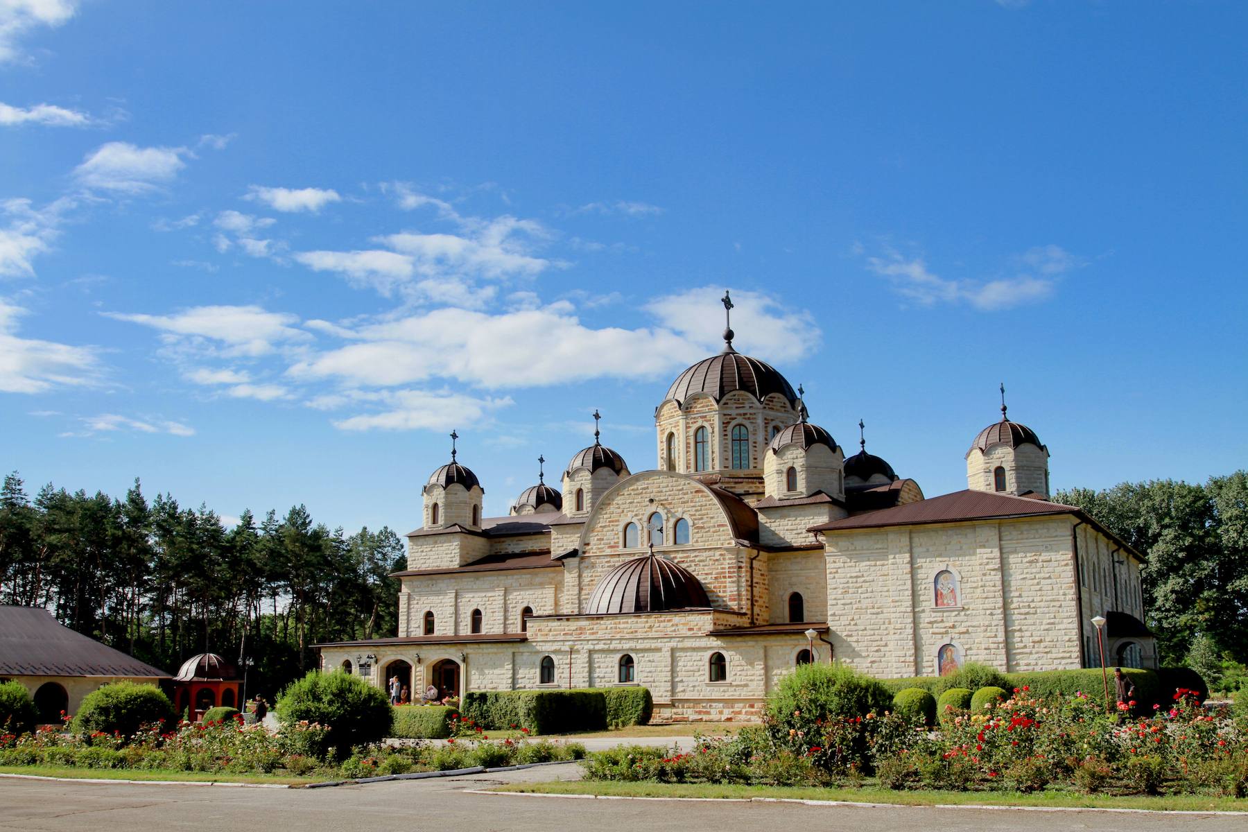 Biserica mănăstirii, din piatră albă cu turle brune, deasupra straturilor de trandafiri